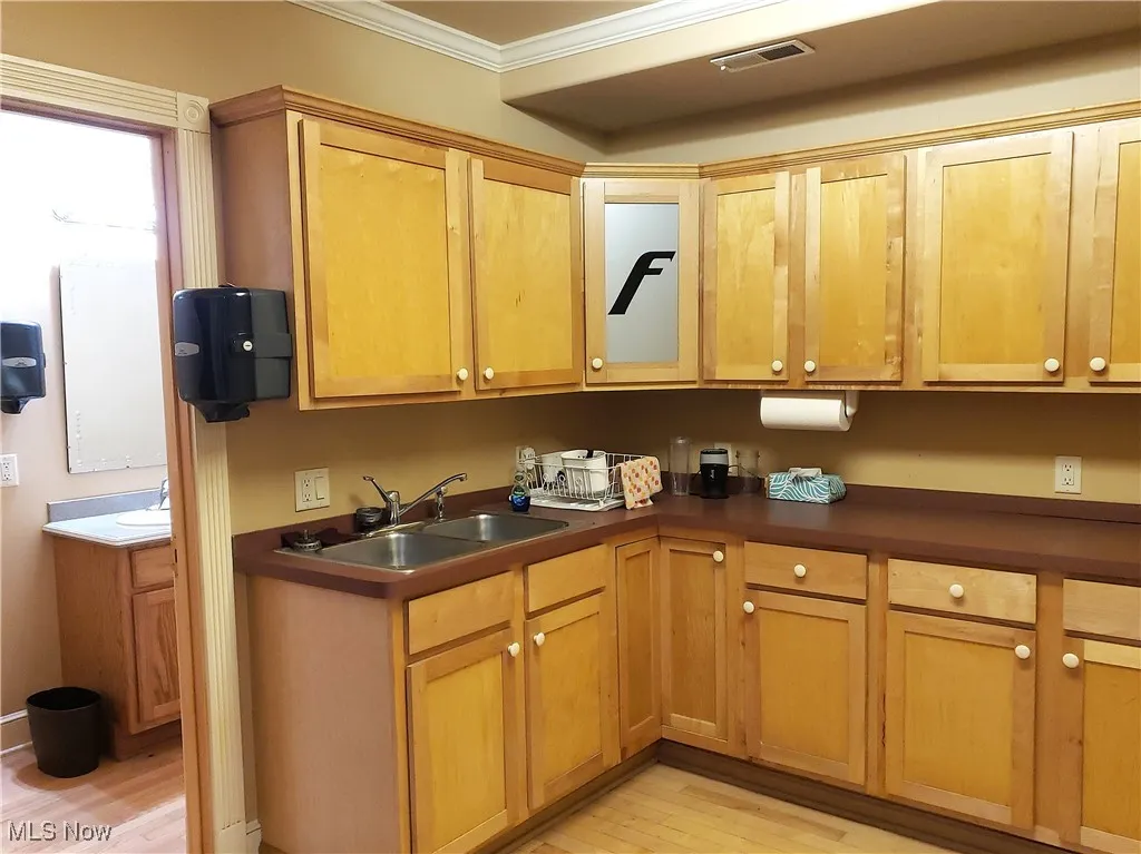 Kitchen featuring dark countertops, light wood-style floors, crown molding, and brown cabinets