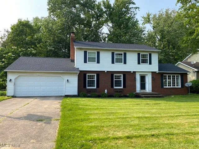 Colonial inspired home with an attached garage, a chimney, concrete driveway, and a front lawn