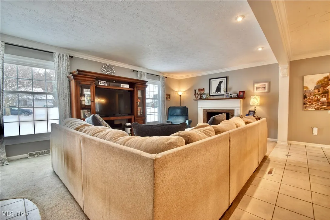 Living room with a fireplace, crown molding, a textured ceiling, light tile patterned floors, and recessed lighting