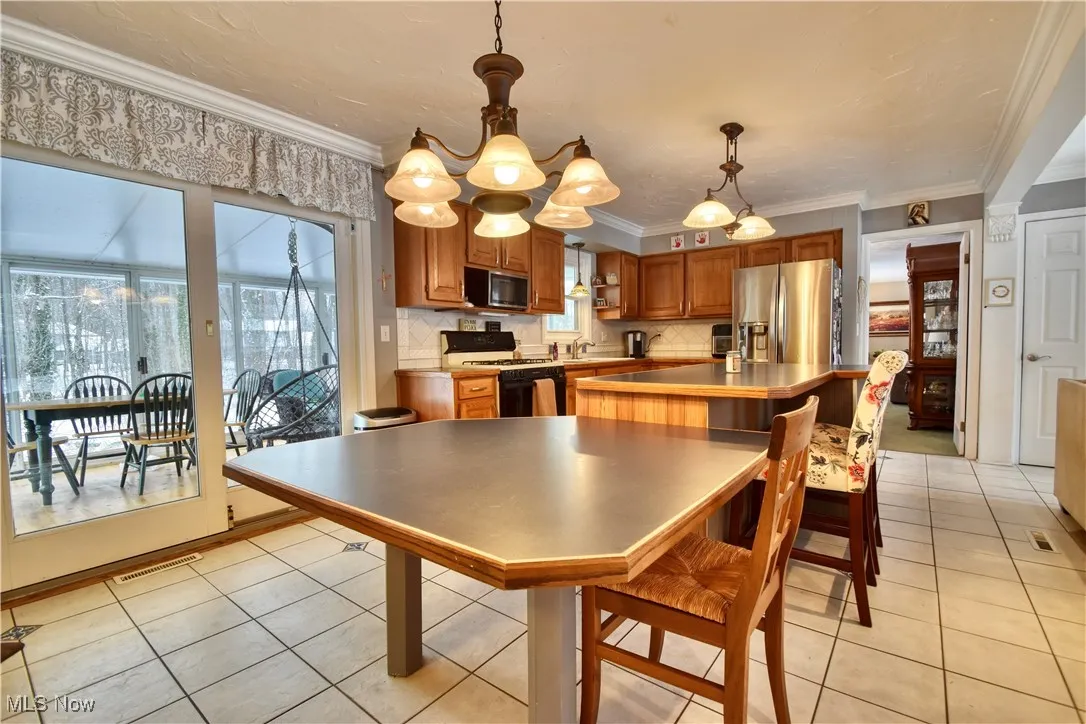 Kitchen with light countertops, appliances with stainless steel finishes, light tile patterned floors, pendant lighting, and ornamental molding