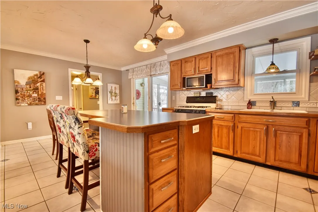 Kitchen featuring brown cabinetry, backsplash, ornamental molding, a kitchen breakfast bar, and a center island