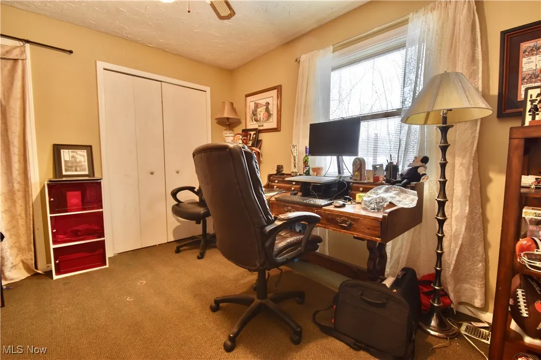 Home office with a textured ceiling, carpet flooring, and a ceiling fan