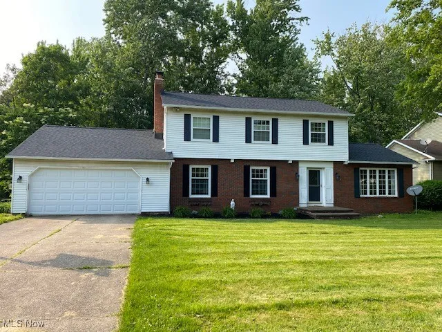 Colonial house featuring a garage, a chimney, concrete driveway, and a front lawn