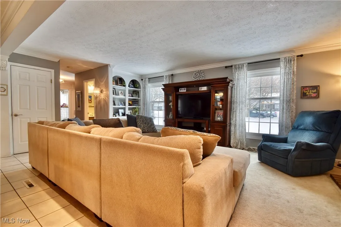 Living area with ornamental molding, a textured ceiling, healthy amount of natural light, and light tile patterned floors