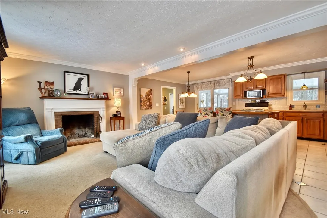 Living room featuring a brick fireplace, a chandelier, ornamental molding, and a textured ceiling