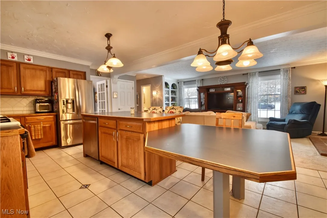 Kitchen with brown cabinets, hanging light fixtures, open floor plan, ornamental molding, and a textured ceiling