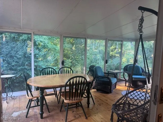Sunroom featuring wood-type flooring, expansive windows, outdoor dining area, and view of wooded area