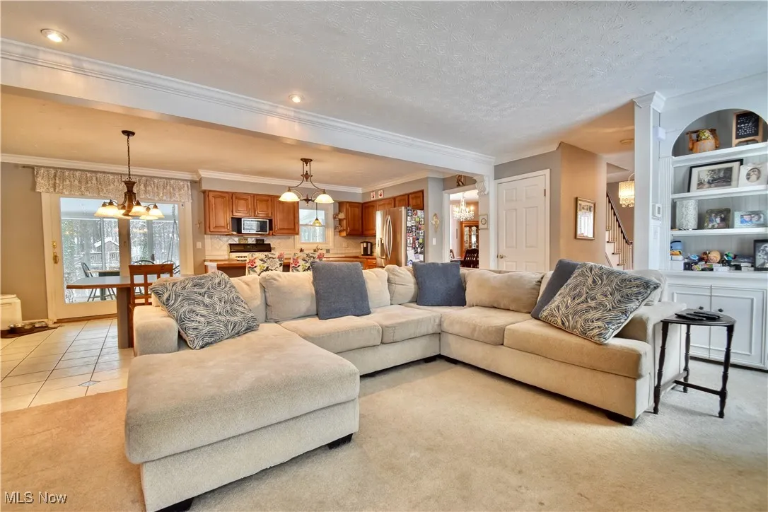 Living area with a chandelier, ornamental molding, light carpet, a textured ceiling, and light tile patterned floors