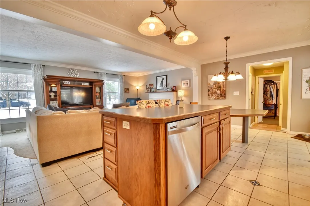 Kitchen featuring stainless steel dishwasher, pendant lighting, light tile patterned flooring, open floor plan, and brown cabinetry