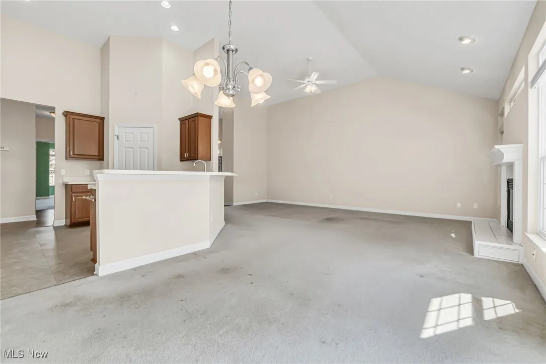 Unfurnished living room with light carpet, a chandelier, recessed lighting, a ceiling fan, and high vaulted ceiling