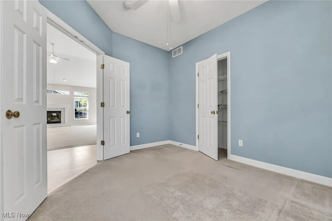 Unfurnished bedroom with carpet flooring, a glass covered fireplace, and ceiling fan