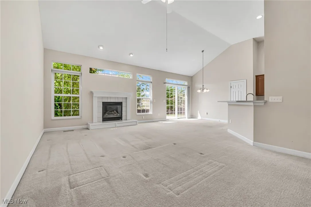 Unfurnished living room with high vaulted ceiling, plenty of natural light, light colored carpet, a tiled fireplace, and recessed lighting