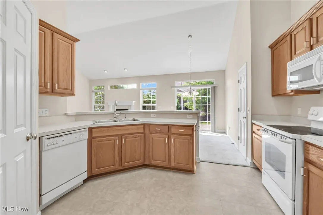 Kitchen with white appliances, a peninsula, light countertops, and brown cabinetry