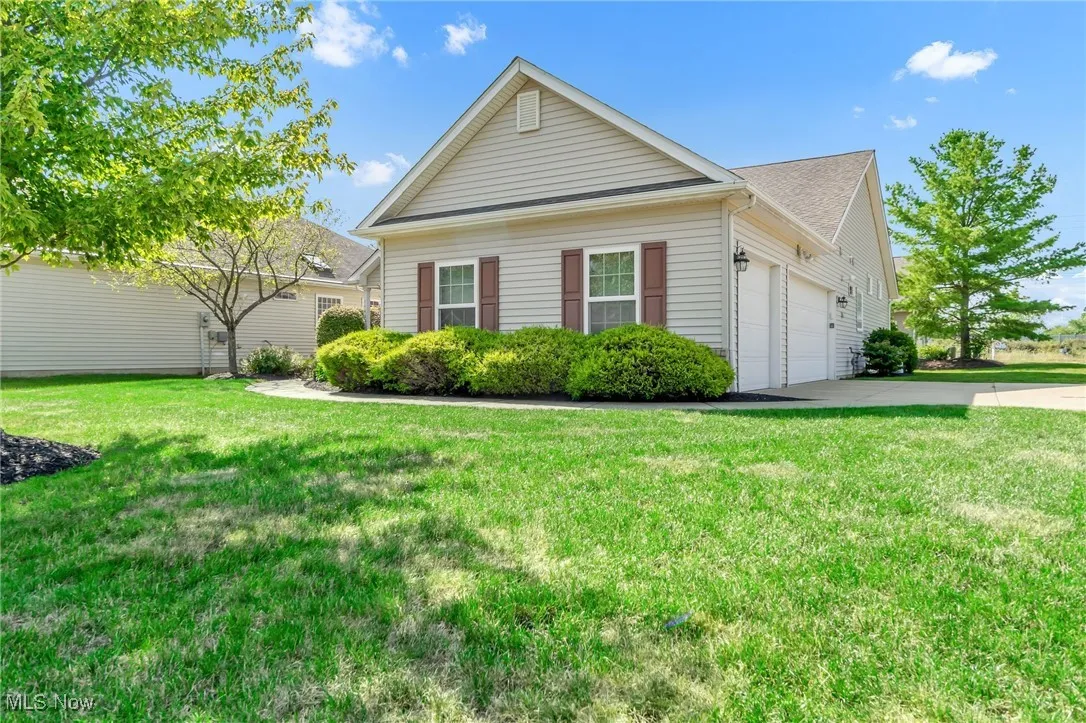 View of side of property featuring driveway, a garage, a yard, and roof with shingles