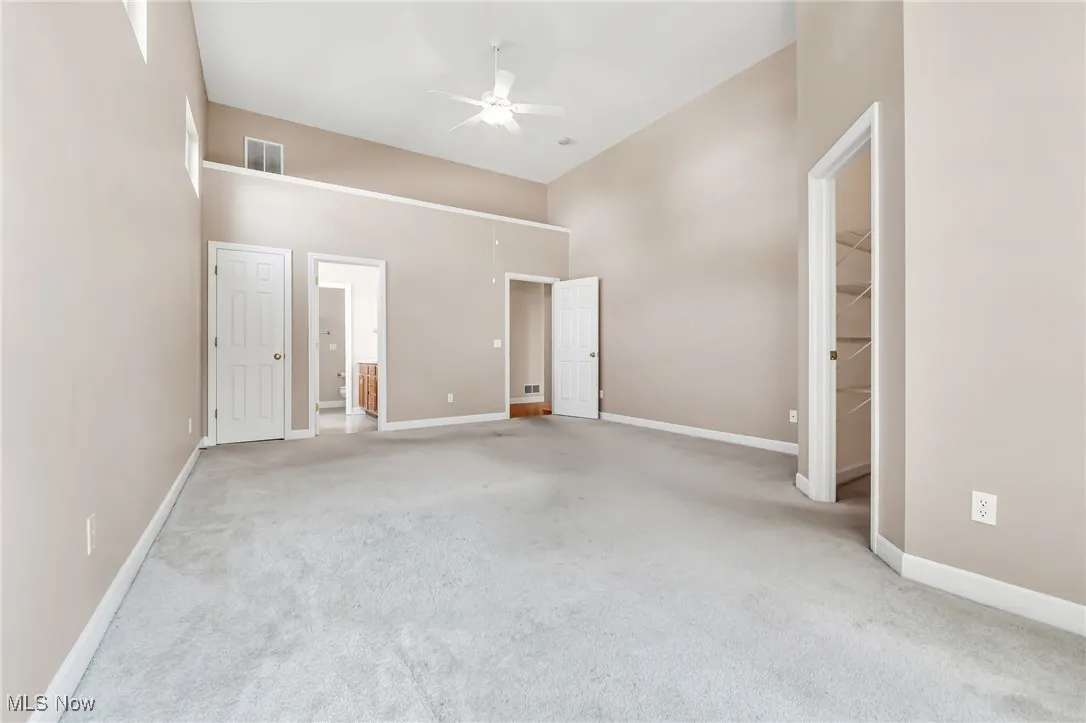 Unfurnished bedroom featuring carpet floors, a walk in closet, ceiling fan, a high ceiling, and connected bathroom
