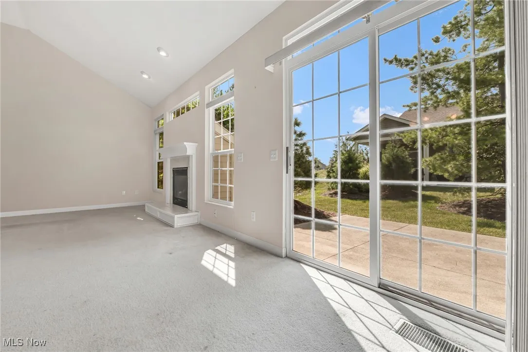 Unfurnished living room with a glass covered fireplace, light colored carpet, high vaulted ceiling, and recessed lighting