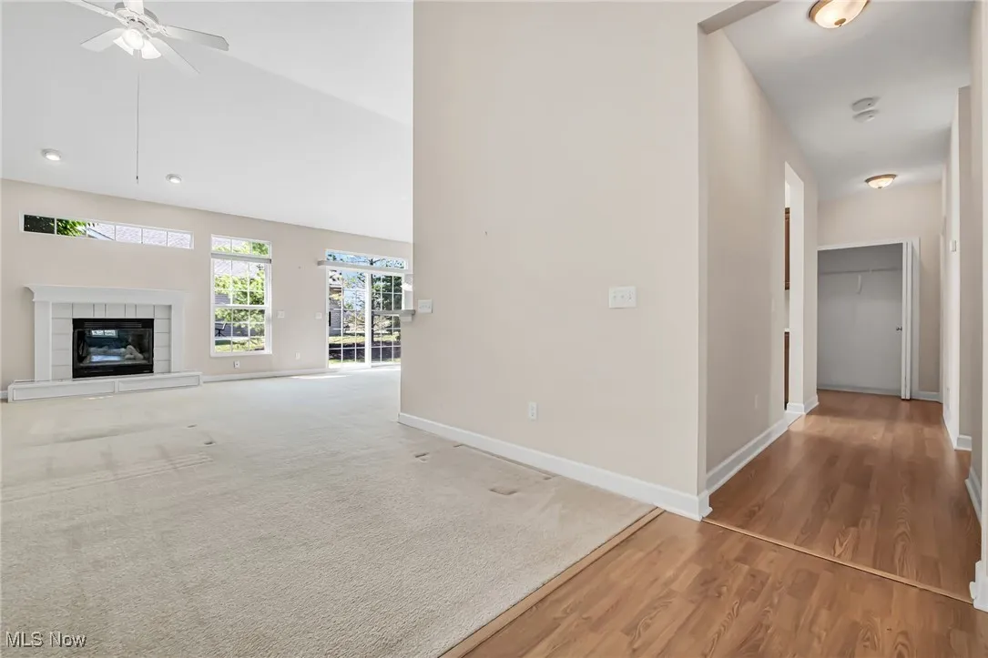 Unfurnished living room featuring a ceiling fan, light wood-style flooring, light colored carpet, high vaulted ceiling, and a fireplace