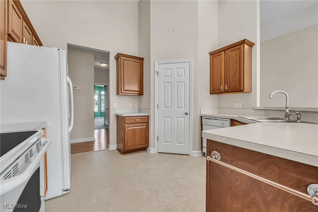 Kitchen featuring brown cabinets, a towering ceiling, light countertops, and white appliances