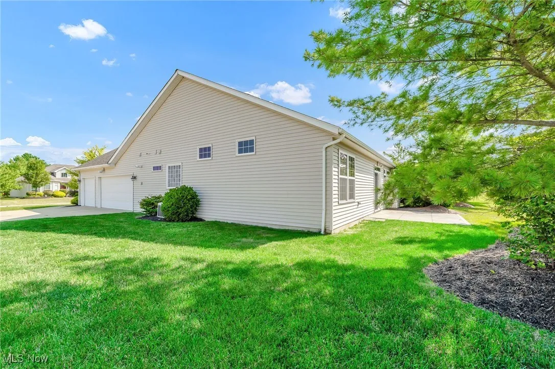 View of side of property featuring a lawn, concrete driveway, an attached garage, and a patio area