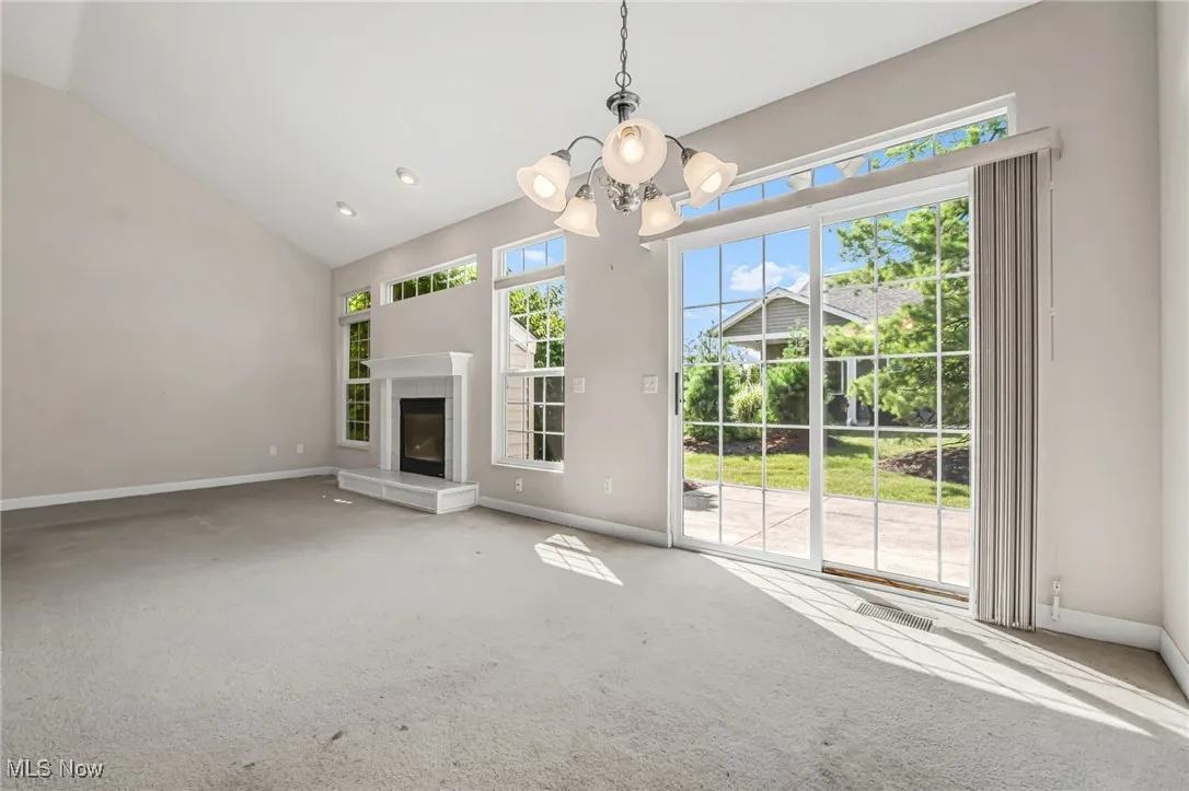 Unfurnished living room with carpet flooring, a chandelier, a glass covered fireplace, high vaulted ceiling, and recessed lighting