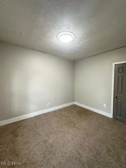 Carpeted empty room with a textured ceiling and baseboards