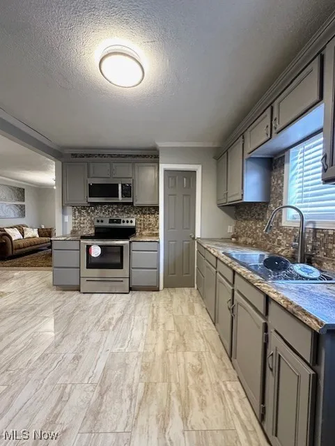 Kitchen featuring gray cabinets, appliances with stainless steel finishes, open floor plan, decorative backsplash, and a textured ceiling