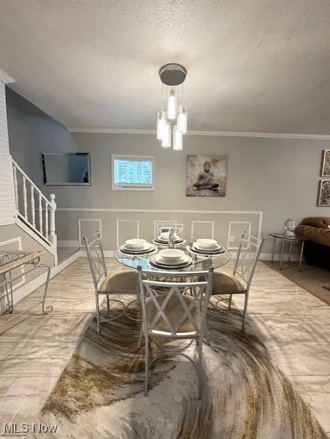 Dining room featuring a textured ceiling, ornamental molding, stairs, and a chandelier