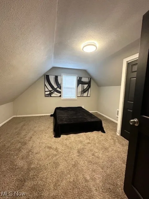 Carpeted bedroom featuring a textured ceiling and vaulted ceiling