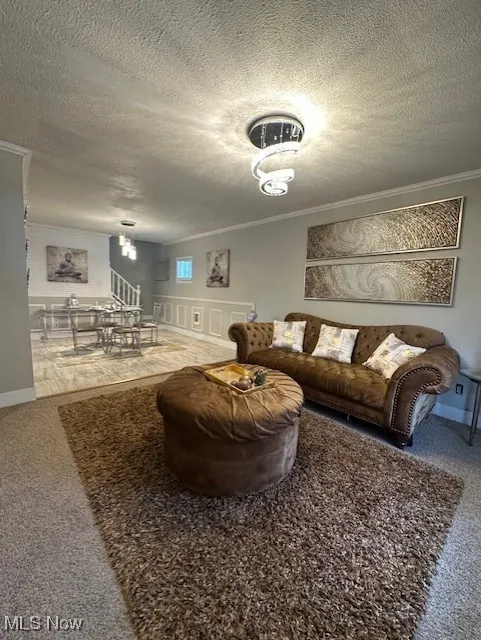 Living room featuring a textured ceiling, crown molding, carpet flooring, and stairway