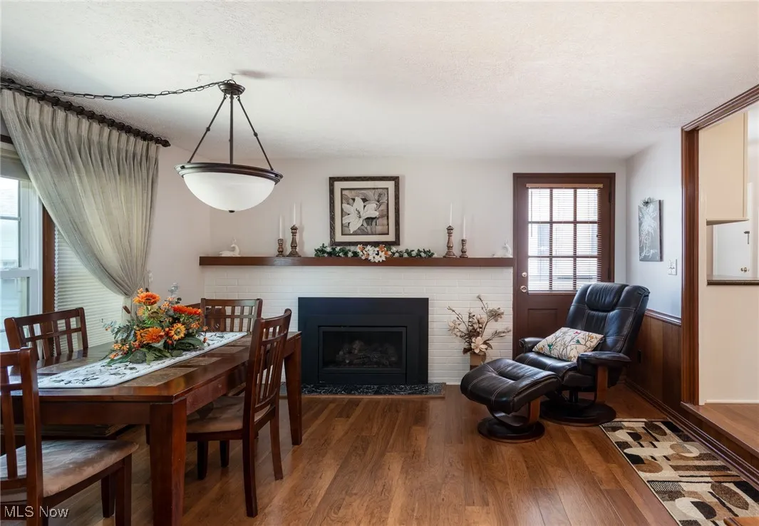 Dining space featuring wood finished floors, a fireplace, a textured ceiling, and a wainscoted wall
