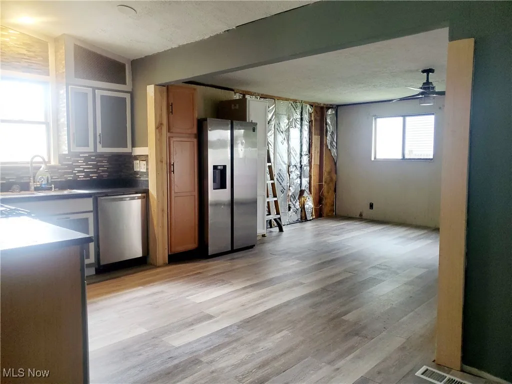 Kitchen with appliances with stainless steel finishes, light wood-style flooring, dark countertops, a ceiling fan, and backsplash
