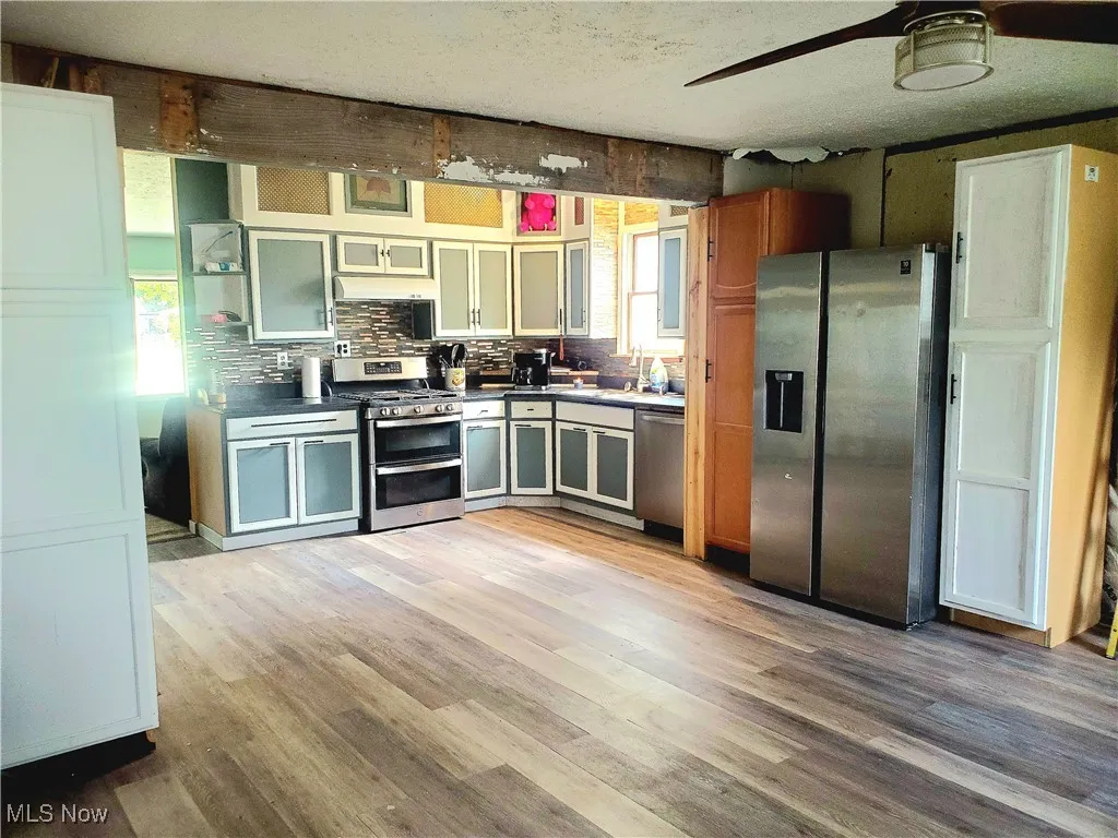 Kitchen featuring dark countertops, stainless steel appliances, light wood-type flooring, open shelves, and backsplash