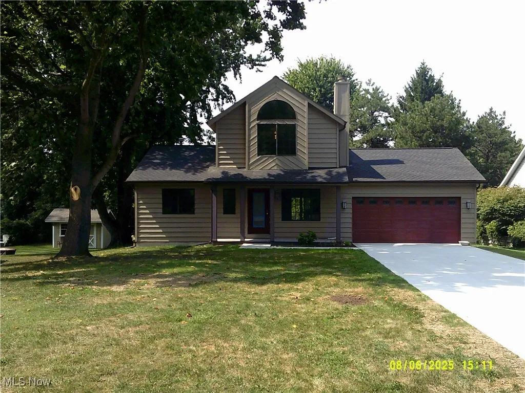 View of front facade with an attached garage, concrete driveway, a chimney, a front yard, and roof with shingles