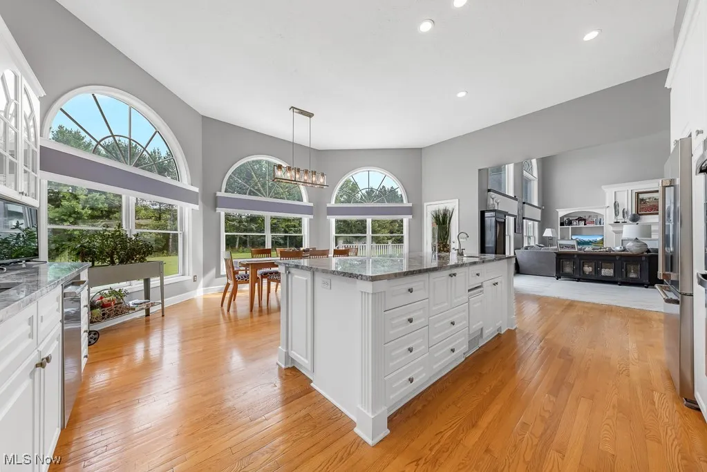 Kitchen with white cabinets, hanging light fixtures, dark stone countertops, an island with sink, and light wood-style flooring