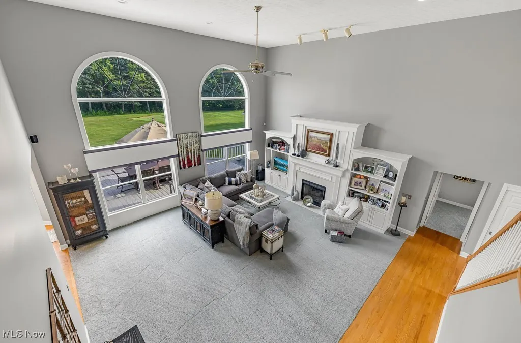 Living area with wood finished floors, a glass covered fireplace, a ceiling fan, a high ceiling, and a textured ceiling
