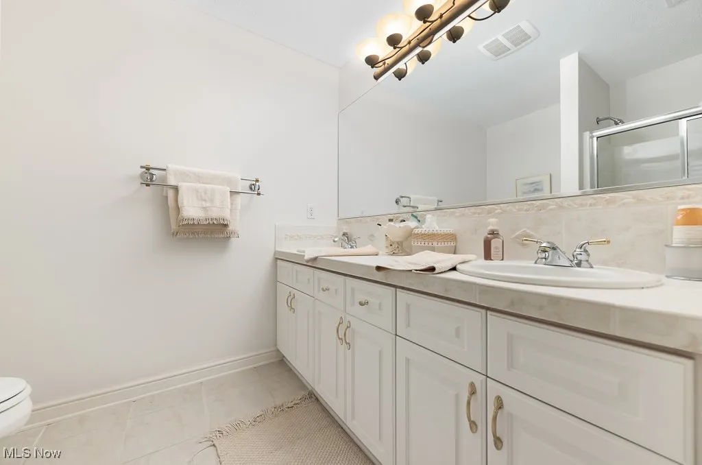 Full bathroom featuring double vanity, a stall shower, light tile patterned floors, and decorative backsplash
