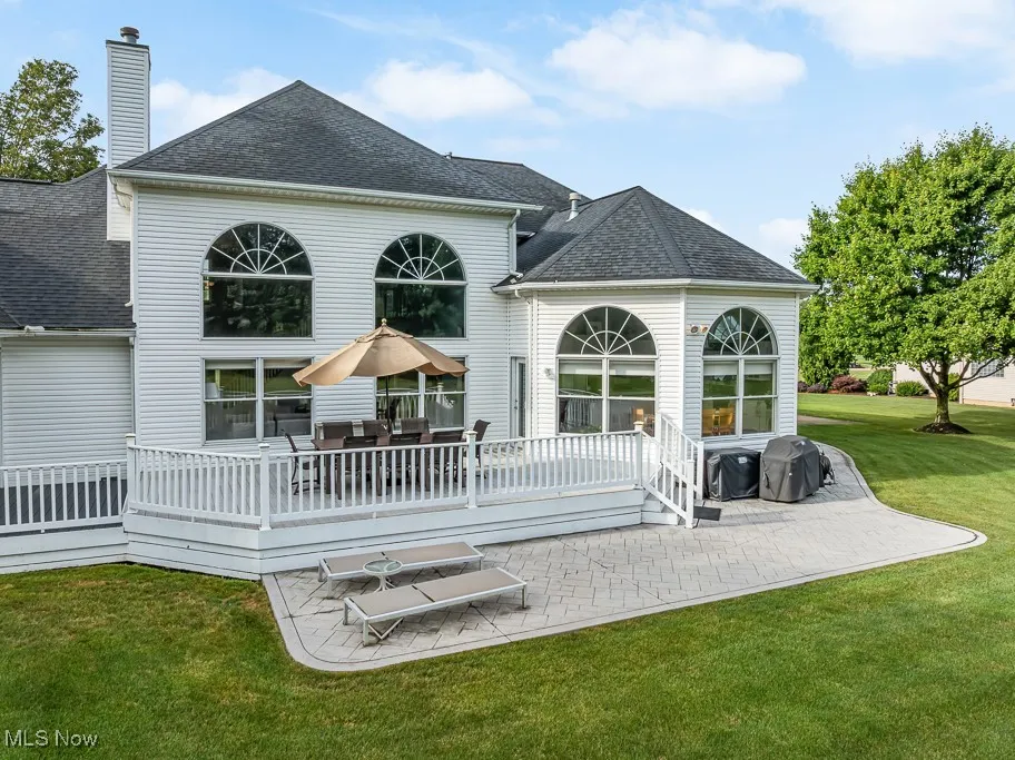 Back of house with a shingled roof, a lawn, a deck, a chimney, and a patio area