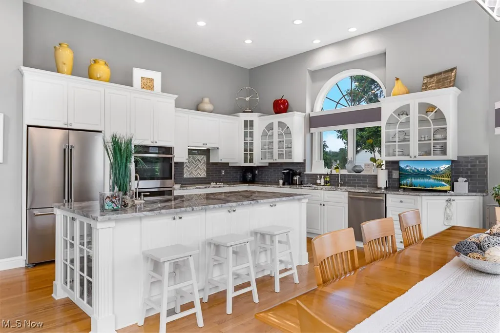 Kitchen featuring glass insert cabinets, white cabinets, stainless steel appliances, light stone counters, and a breakfast bar area