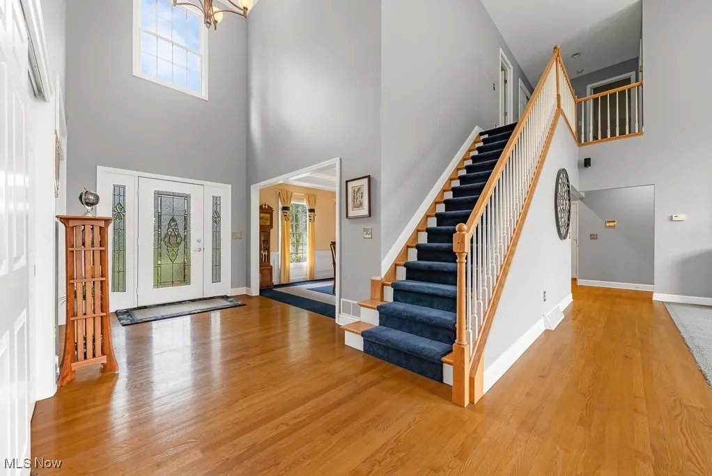Foyer entrance with a high ceiling, light wood finished floors, a chandelier, and stairs