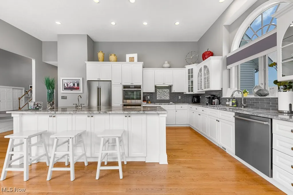 Kitchen with glass insert cabinets, white cabinetry, light stone counters, stainless steel appliances, and recessed lighting