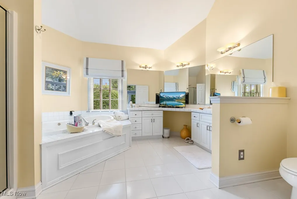 Bathroom with a bath, vanity, light tile patterned floors, plenty of natural light, and lofted ceiling