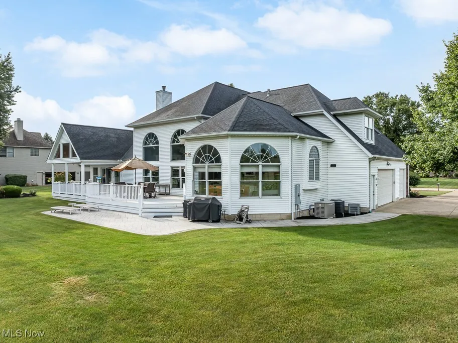 Rear view of property featuring a lawn, a patio, a shingled roof, and driveway