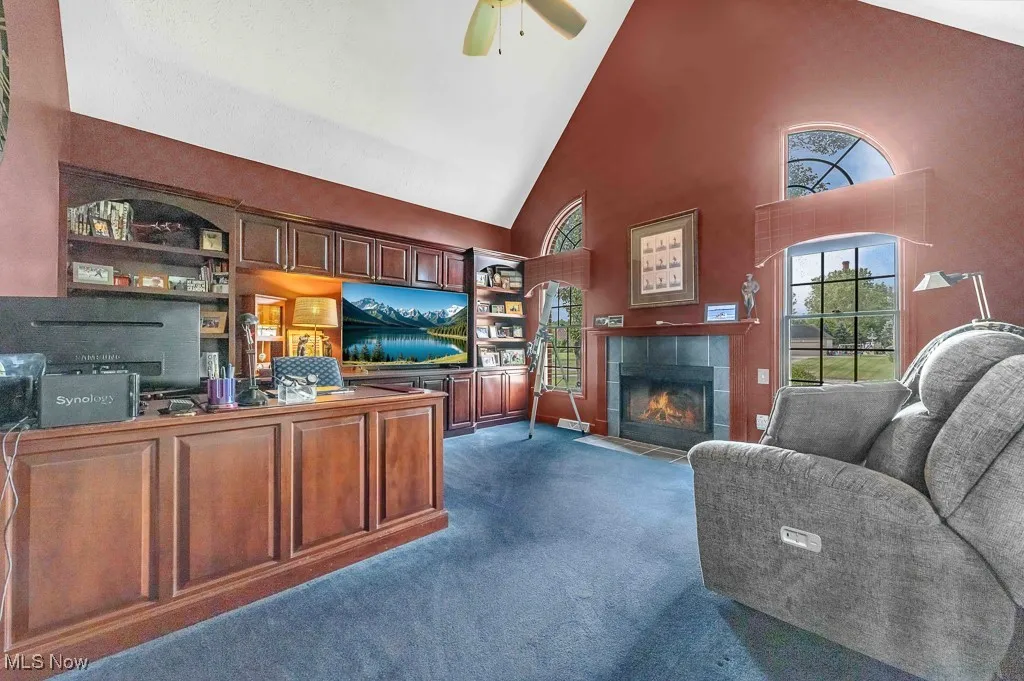 Living area with high vaulted ceiling, dark colored carpet, a fireplace, and ceiling fan