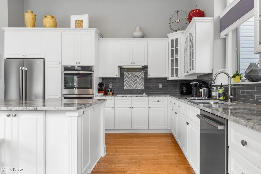 Kitchen with light stone counters, appliances with stainless steel finishes, tasteful backsplash, white cabinets, and light wood-style flooring