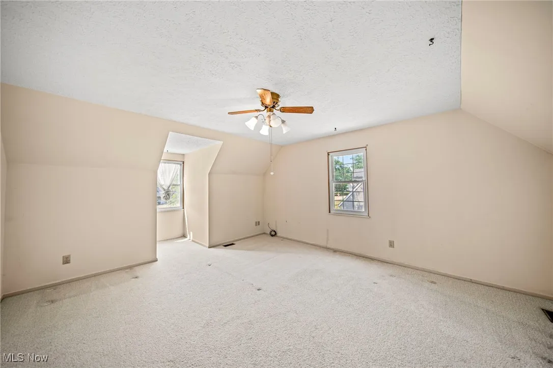 Bonus room featuring vaulted ceiling, carpet, a textured ceiling, and ceiling fan
