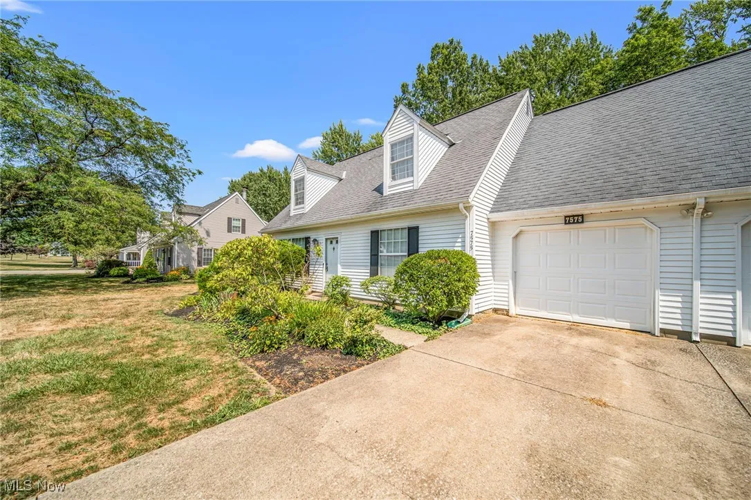 New england style home with concrete driveway, an attached garage, a shingled roof, and a front yard