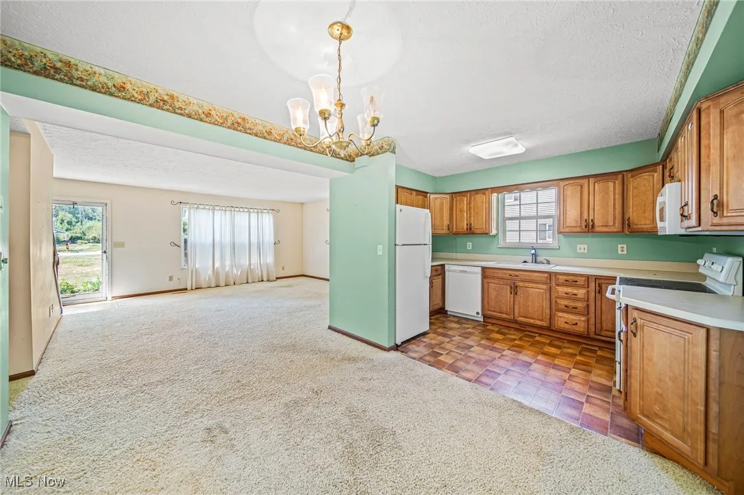 Kitchen with brown cabinetry, light countertops, white appliances, a textured ceiling, and a chandelier