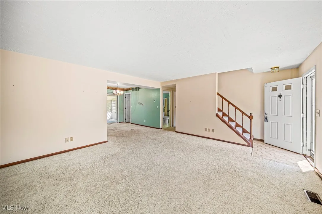 Unfurnished living room featuring stairway, carpet, a chandelier, and a textured ceiling