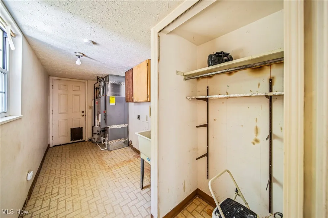 Laundry area featuring brick patterned floors, cabinet space, a textured ceiling, and heating unit