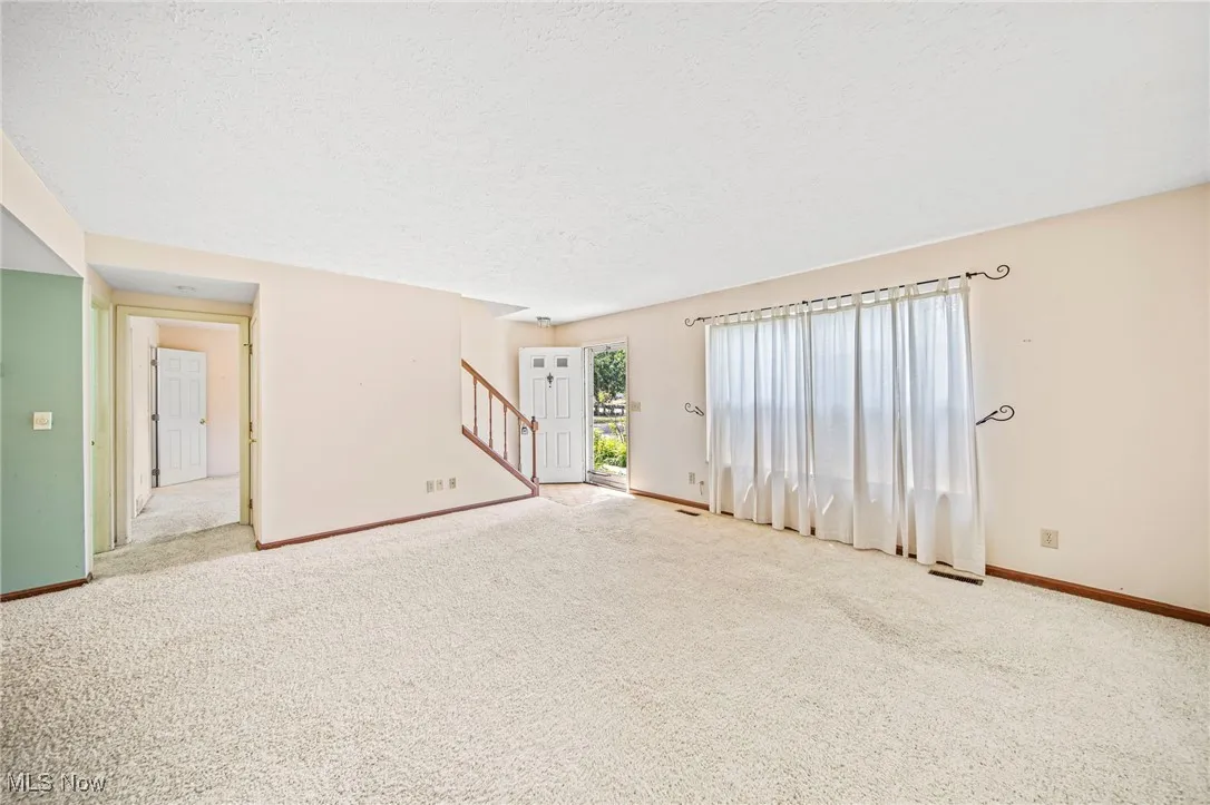 Empty room featuring carpet flooring, stairs, and a textured ceiling